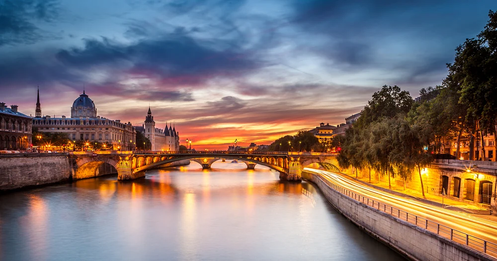 Long-exposure photograph of the Seine River at twilight in Paris, featuring the Conciergerie and vibrant sunset colors reflected in the water.