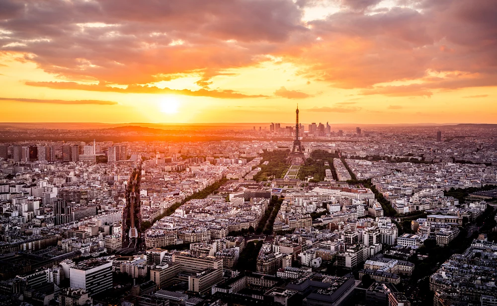 Aerial view of the Eiffel Tower at sunset from Montparnasse Tower, showcasing vibrant colors in the sky and the Paris cityscape.