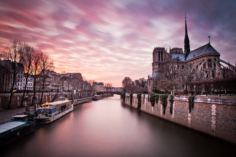Sunset view of Notre-Dame Cathedral in Paris, with the Seine River reflecting vibrant colors in the sky.