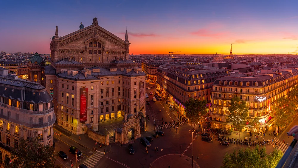 Panoramic view of Paris at sunset featuring the Palais Garnier and Eiffel Tower, showcasing the city's vibrant atmosphere and architectural beauty.