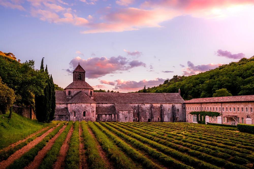 S&eacute;nanque Abbey at sunset surrounded by lavender fields, showcasing medieval architecture and a vibrant sky in Provence, France.