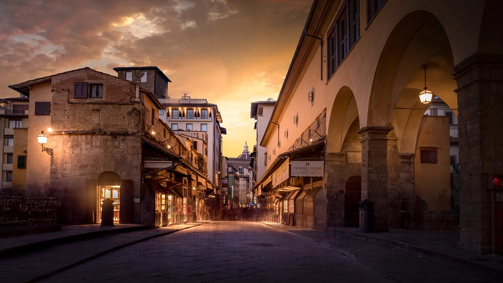 A stunning sunset view of the Ponte Vecchio in Florence, showcasing historic buildings and warm evening light illuminating the cobblestone streets.