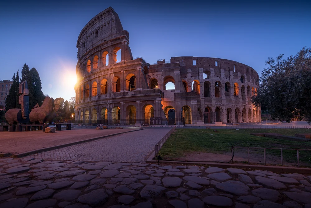 A stunning view of the Colosseum in Rome at sunrise, showcasing the warm glow of morning light illuminating the ancient structure and surrounding greenery.