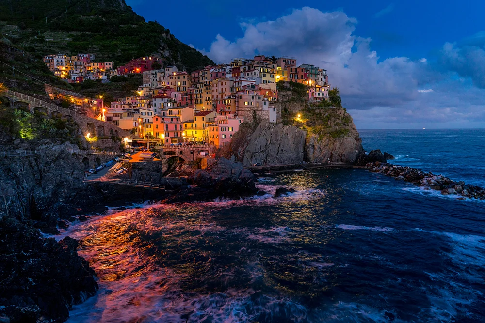 A twilight view of Manarola, Cinque Terre, showcasing colorful buildings illuminated against the deep blue waters of the Ligurian Sea.