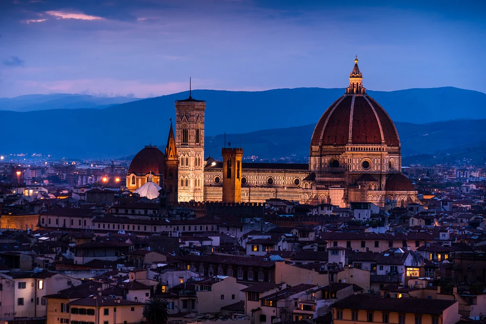 Twilight view of Florence's Duomo and Giotto's Campanile, showcasing the city's historic architecture and warm city lights against a blue sky.
