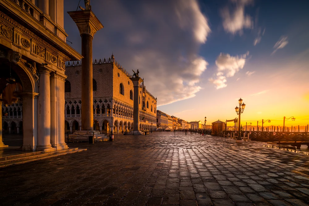 A breathtaking view of St. Mark's Square in Venice at sunrise, showcasing the Doge's Palace and glistening cobblestones reflecting the morning light.