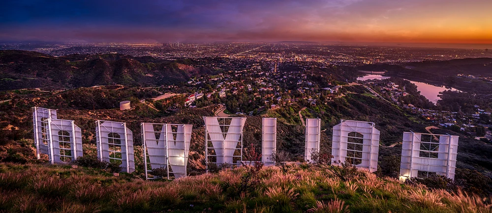 Panoramic view of the Hollywood Sign at sunset, showcasing the vibrant colors of the evening sky and the sprawling Los Angeles skyline in the background.