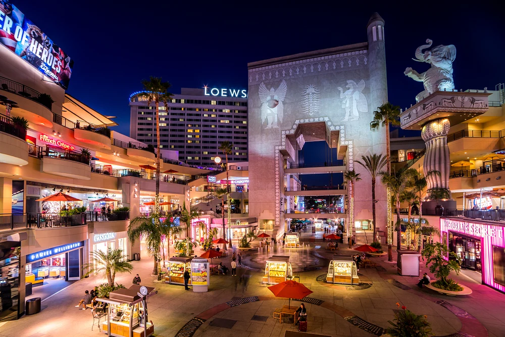 A vibrant night view of the Hollywood Walk of Fame, featuring illuminated storefronts, the Loews hotel, and artistic sculptures, capturing the lively atmosphere of this famous entertainment district.