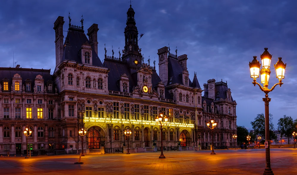 Twilight view of Hotel de Ville in Paris, showcasing its intricate architecture and illuminated street lamps against a darkening sky.