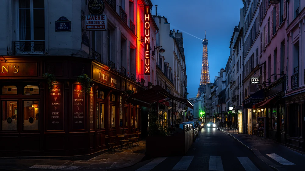 A picturesque Parisian street at dusk featuring a glowing bistro and the illuminated Eiffel Tower in the background, capturing the romantic ambiance of the City of Light.