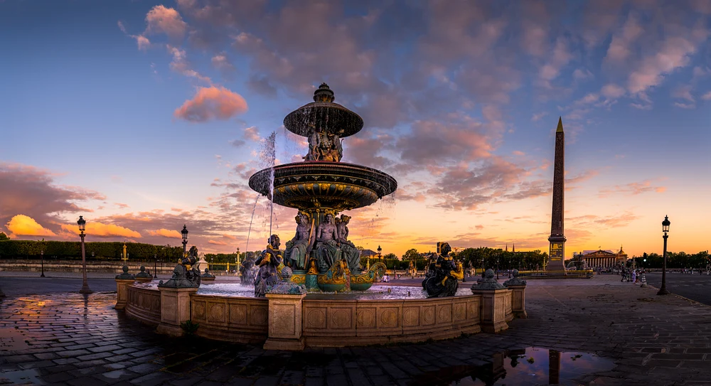 A stunning sunset over the Fontaine des Mers at Place de la Concorde in Paris, showcasing golden and blue hues in the sky, ornate sculptures, and the historic obelisk in the background.