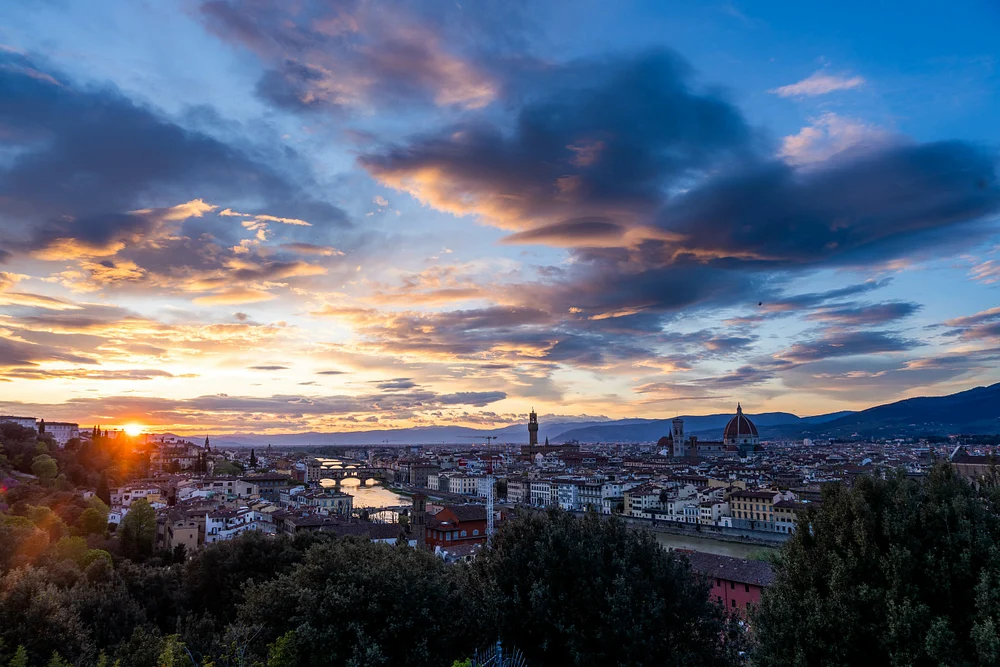 A stunning sunset view over Florence, Italy, showcasing the Arno River, Duomo, and Ponte Vecchio under dramatic clouds.