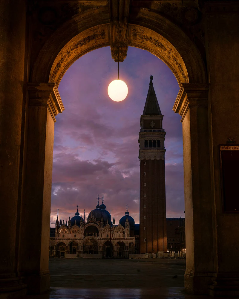 A stunning dusk view of St. Mark's Basilica and Campanile in Venice, framed by an elegant archway, showcasing rich architectural details and a vibrant sky.