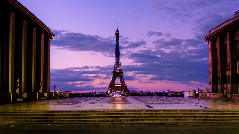 Eiffel Tower illuminated at dusk, framed by Palais de Chaillot, showcasing a vibrant purple and pink sky in Paris.