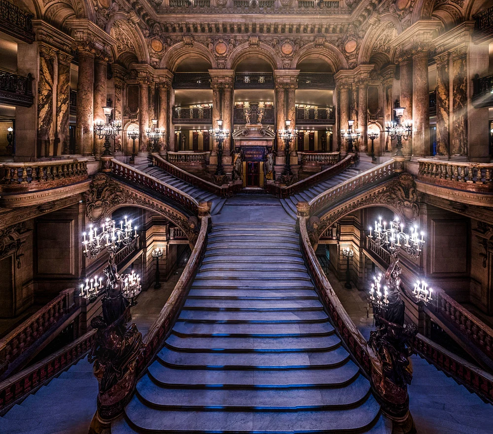 Interior view of the grand staircase at Palais Garnier, Paris Opera House, showcasing ornate chandeliers and intricate architectural details.