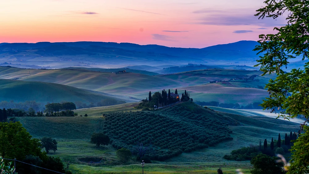 A breathtaking sunrise over the rolling hills of Tuscany, featuring cypress trees and olive groves amidst a misty landscape.