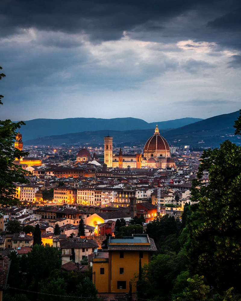 A panoramic view of Florence at dusk, featuring the illuminated Duomo and city lights against a dramatic sky.