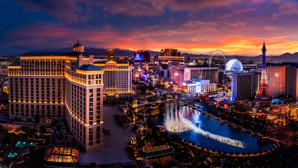 Aerial view of the Las Vegas Strip at sunset, featuring illuminated hotels, the Bellagio fountains, and the High Roller observation wheel.