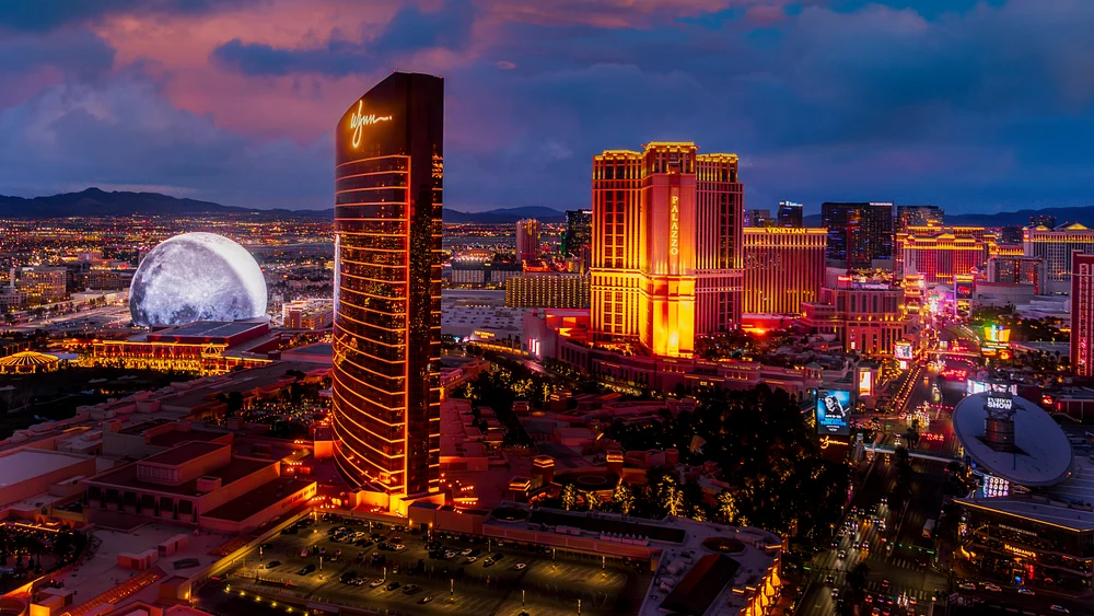 Aerial view of the Las Vegas Strip at dusk, featuring illuminated hotels and the Wynn Las Vegas with a modern Sphere in the background.