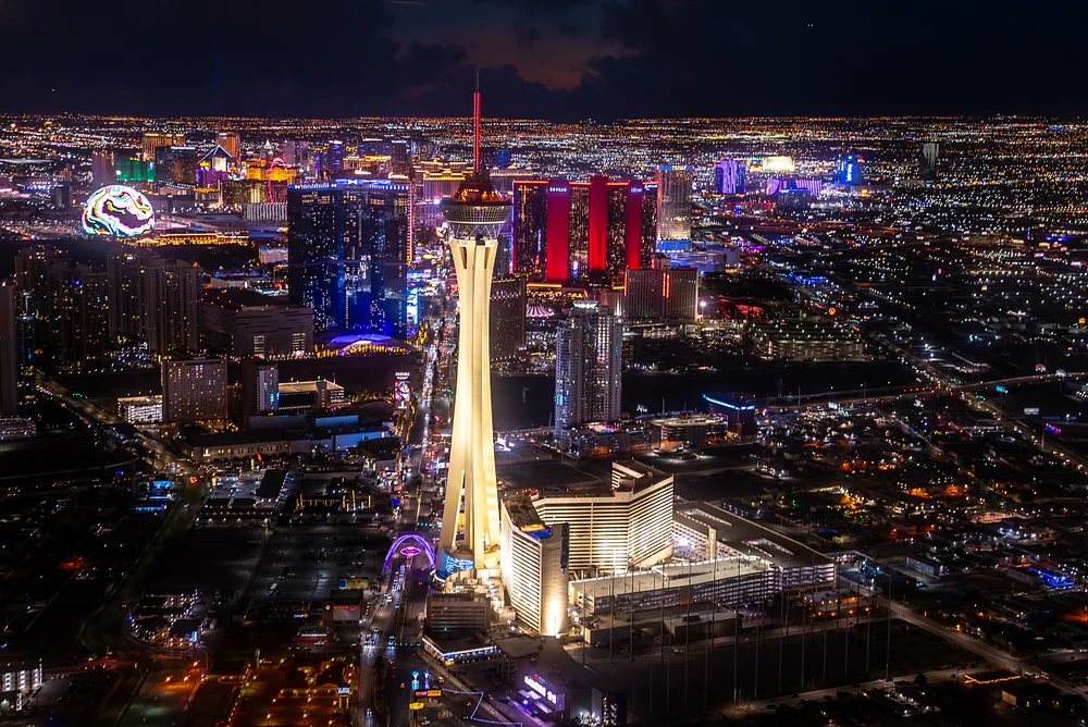 Aerial view of the Las Vegas Strip at night, showcasing the illuminated Stratosphere Tower and vibrant city lights.