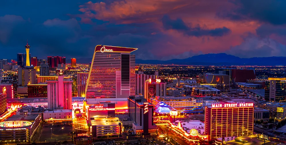 A panoramic view of the Las Vegas Strip at night, showcasing vibrant lights and iconic landmarks against a dramatic sunset backdrop.