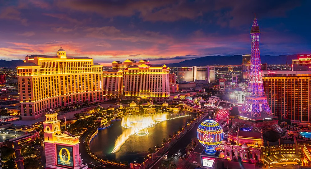 Aerial view of the Las Vegas Strip at sunset, showcasing the illuminated buildings and fountain show at the Bellagio.