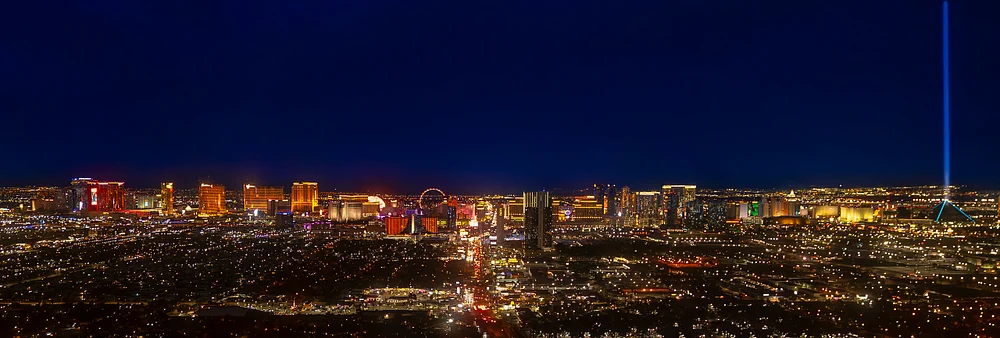 Aerial view of the Las Vegas skyline at night, showcasing illuminated buildings and landmarks against a dark blue sky.