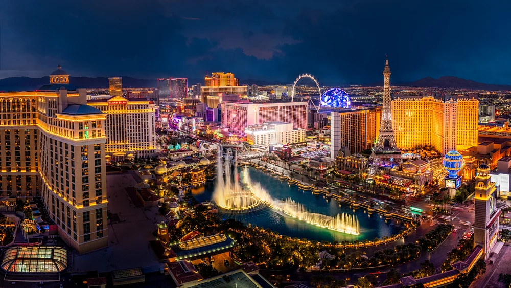 A stunning night view of the Las Vegas Strip, featuring illuminated casinos, the Bellagio fountains, and the Eiffel Tower replica.