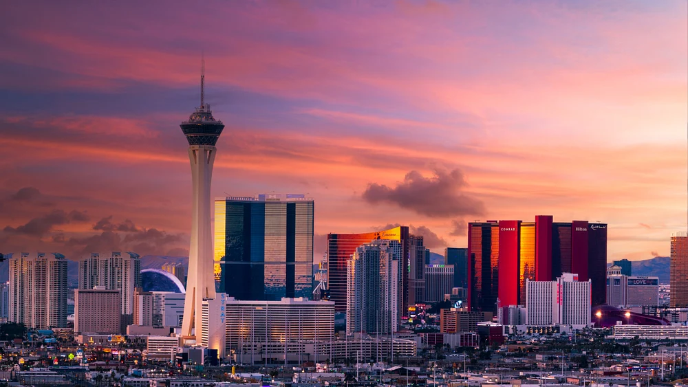 Panoramic view of the Las Vegas skyline at sunset, featuring the Stratosphere Tower and colorful skyscrapers against a dramatic sky.