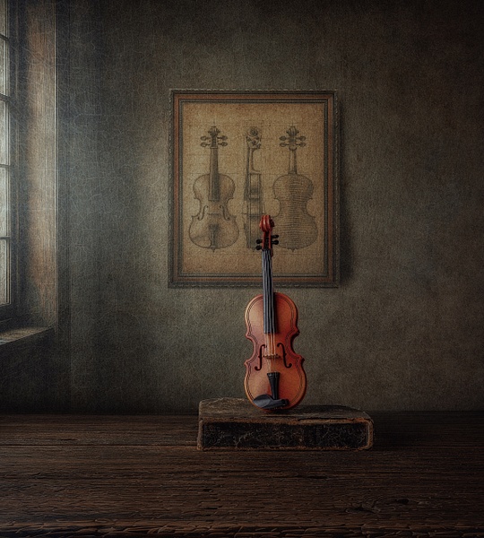 The Last Song by Marko Klavs, a fine art still life photograph of an antique violin resting on an old case beneath a framed illustration of violins in a timeless historic interior, illuminated by soft window light.