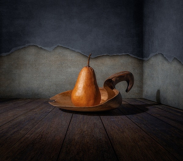 Silent Tension by Marko Klavs, a fine art still life photograph of a single pear resting in a handcrafted wooden vessel against a weathered textured wall, illuminated by directional light.