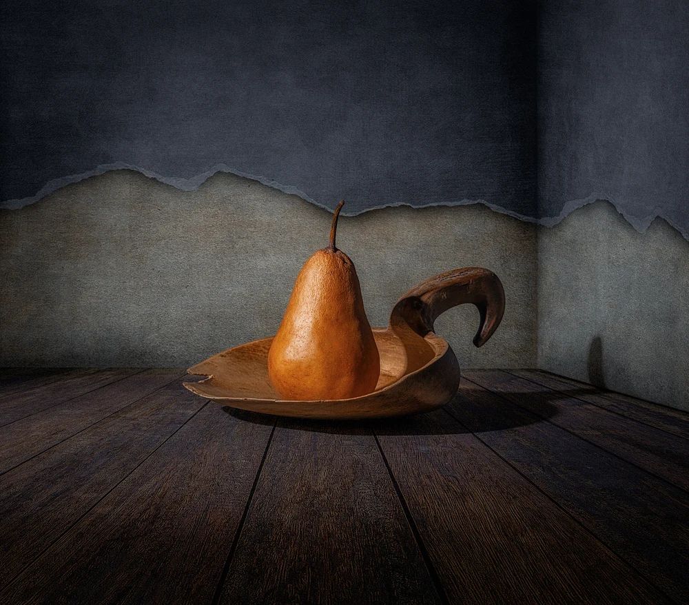 Silent Tension by Marko Klavs, a fine art still life photograph of a single pear resting in a handcrafted wooden vessel against a weathered textured wall, illuminated by directional light.
