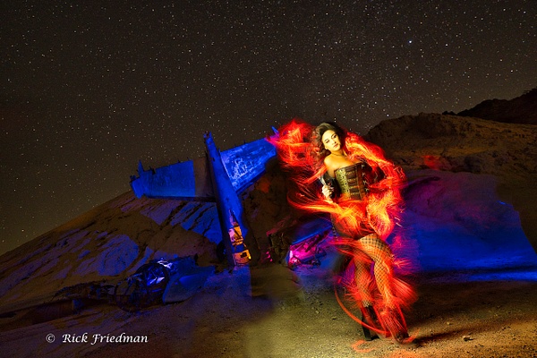 Light painting brunette model surrounded by flames in front of a crashed blue airplane under the stars by Rick Friedman - Models - Rick Friedman Photography