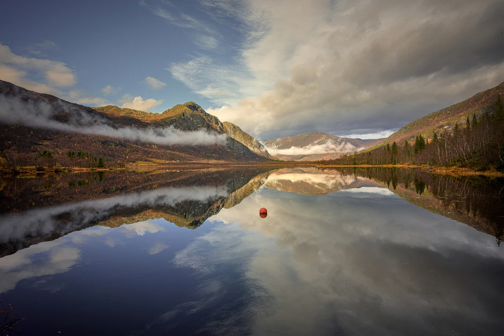 A tranquil view of Fagersetvatnet Lake reflecting autumn mountains and clouds, creating a serene natural landscape.