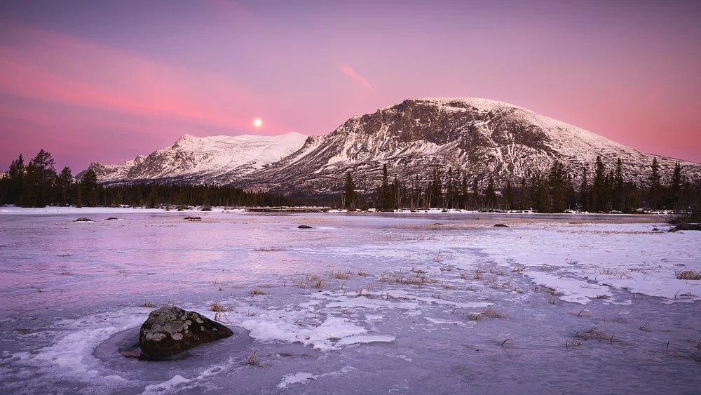 Full moon rising over Nibbi Mountain, illuminating a frozen lake and snow-covered landscape at dusk.