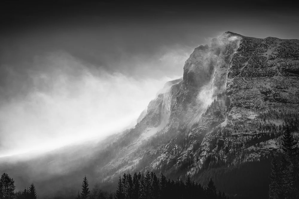Black and white photograph of Veslehorn Mountain during a winter storm, showcasing mist and rugged terrain.