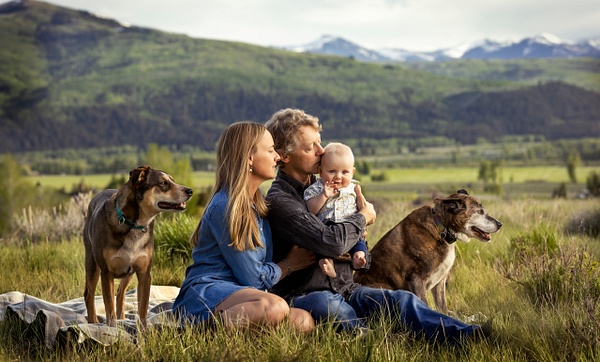 family with baby and dogs sitting in field with mountains - Flo McCall Photography