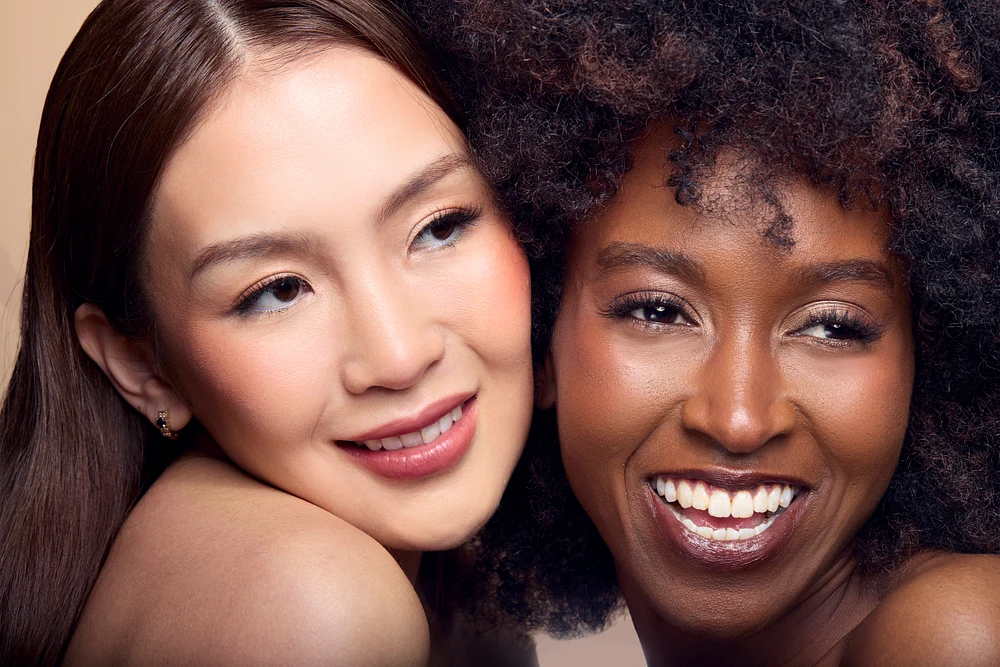 Two women with diverse skin tones smiling together, showcasing natural beauty and friendship.