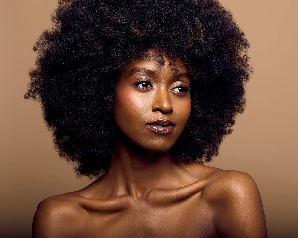 Portrait of a woman with a natural afro hairstyle and glowing skin against a warm background.