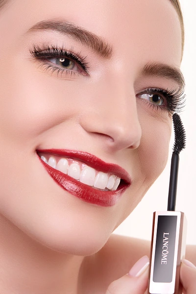 Model smiling while holding mascara tube in a beauty photoshoot.