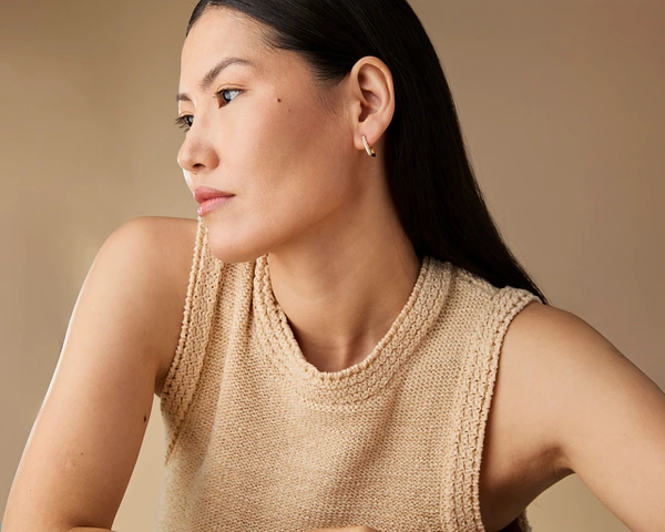 Model showcasing elegant earrings against a neutral background, highlighting beauty and style.