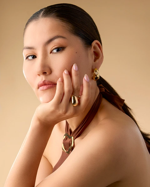 Model displaying elegant gold jewelry with a neutral background, showcasing natural beauty and sophistication.