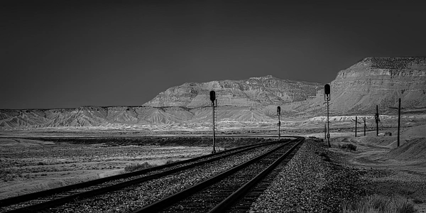 Black-and-white landscape of winding railroad tracks leading toward distant hills near Green River, Utah.