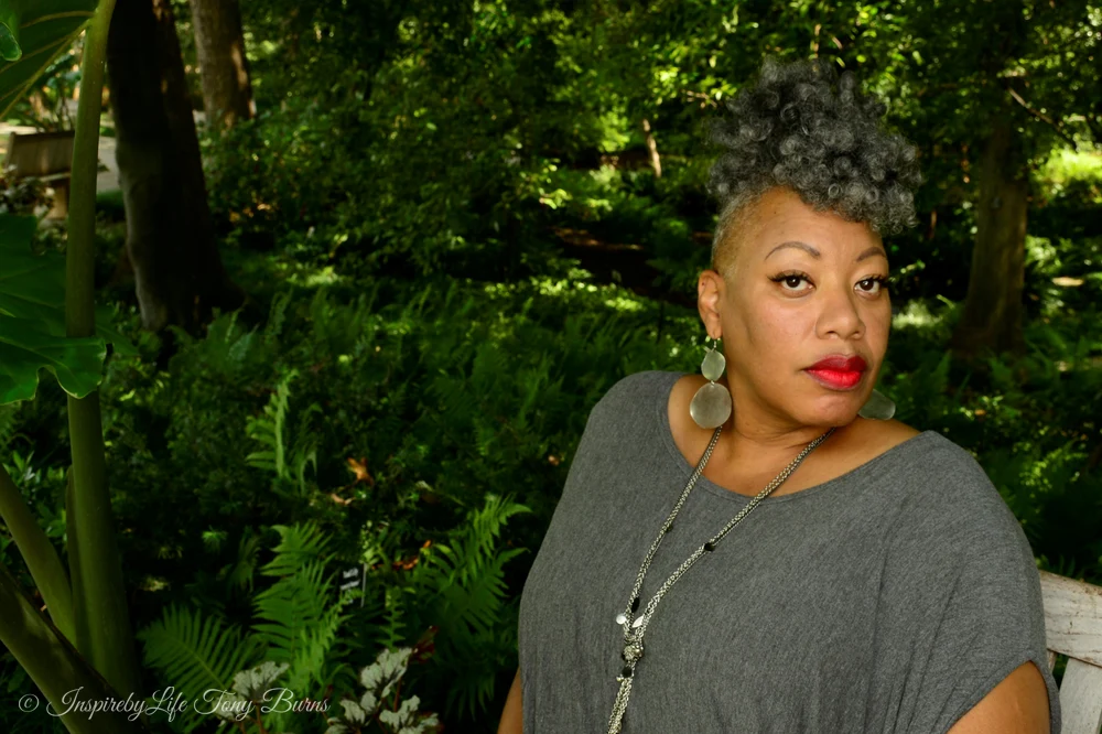 Confident Woman in Stylish Gray Attire Confident woman with unique hairstyle in gray attire surrounded by greenery.