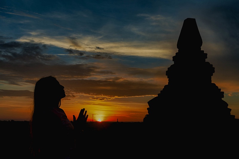 Silhouette of a woman praying at sunrise at a pagoda, Myanmar