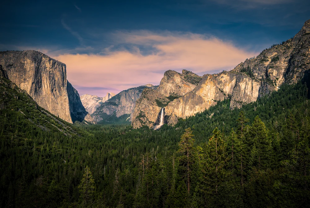 A stunning view of Yosemite Valley featuring granite cliffs and a waterfall under colorful skies.
