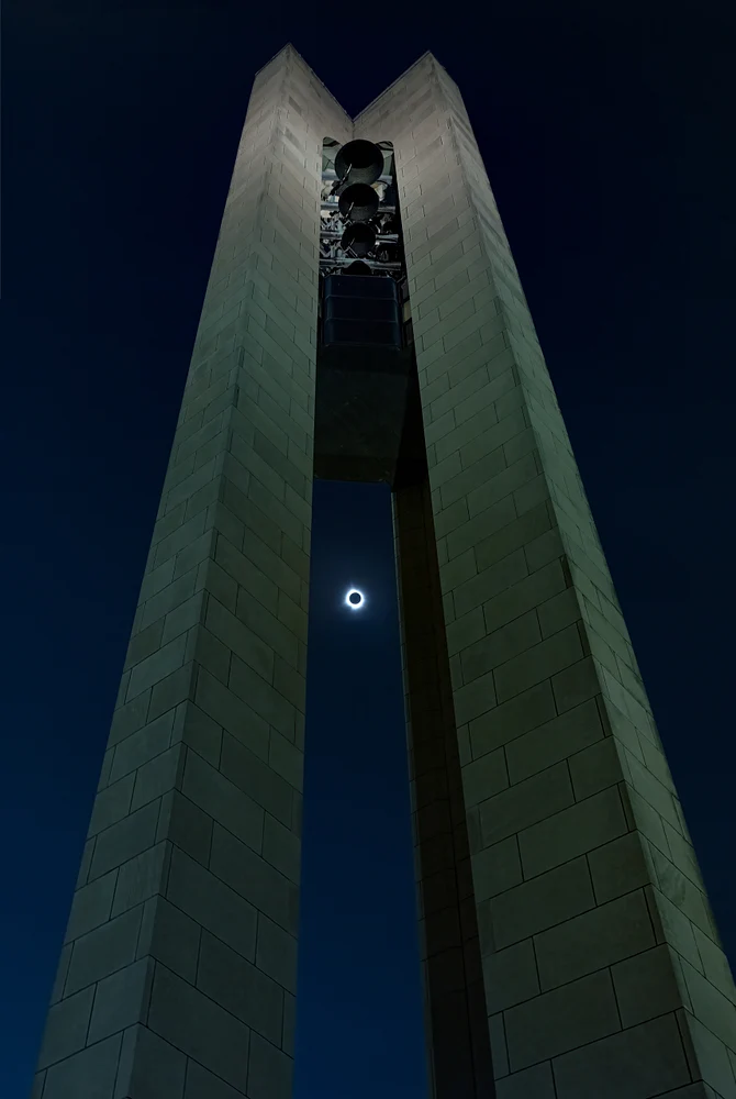 A striking solar eclipse visible through a tall monument at night.