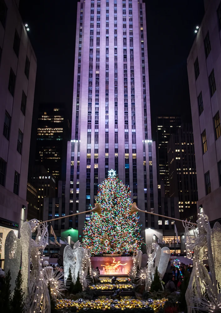 Vibrant Christmas tree at Rockefeller Center illuminated at night with angel sculptures.