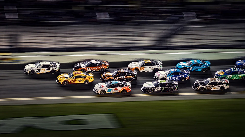Dynamic scene from Coke Zero Sugar 400 showing multiple NASCAR cars racing closely on a lit track.
