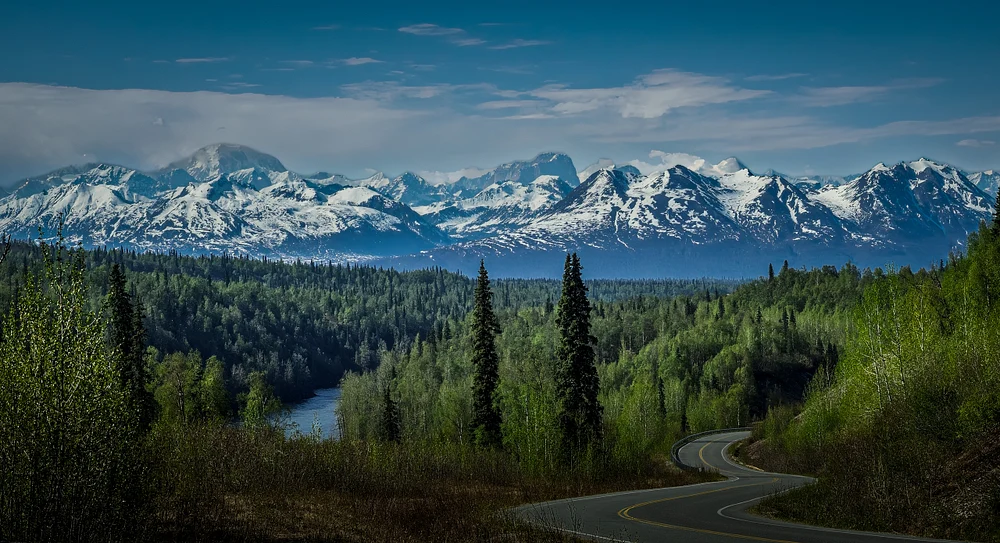 Scenic view of snow-covered mountains with a winding road and river in Alaska.